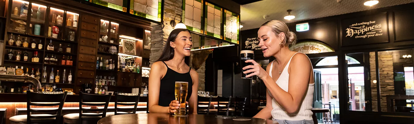 One brunette female and one blonde female sitting around a table at Finn McCools. With beers in hand. 