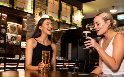 One brunette female and one blonde female sitting around a table at Finn McCools. With beers in hand. 