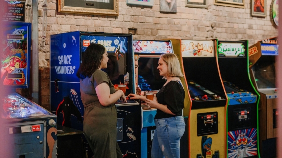 Two girls standing holding beers in front of arcade machines