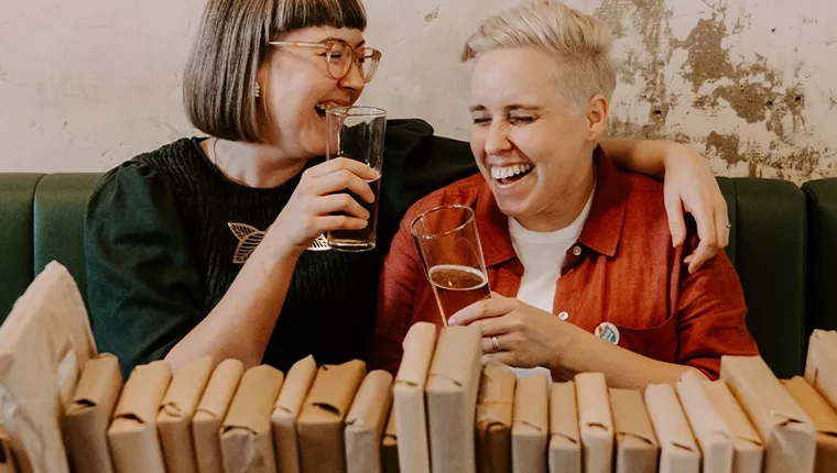 two friends laughing with a selection of books in front